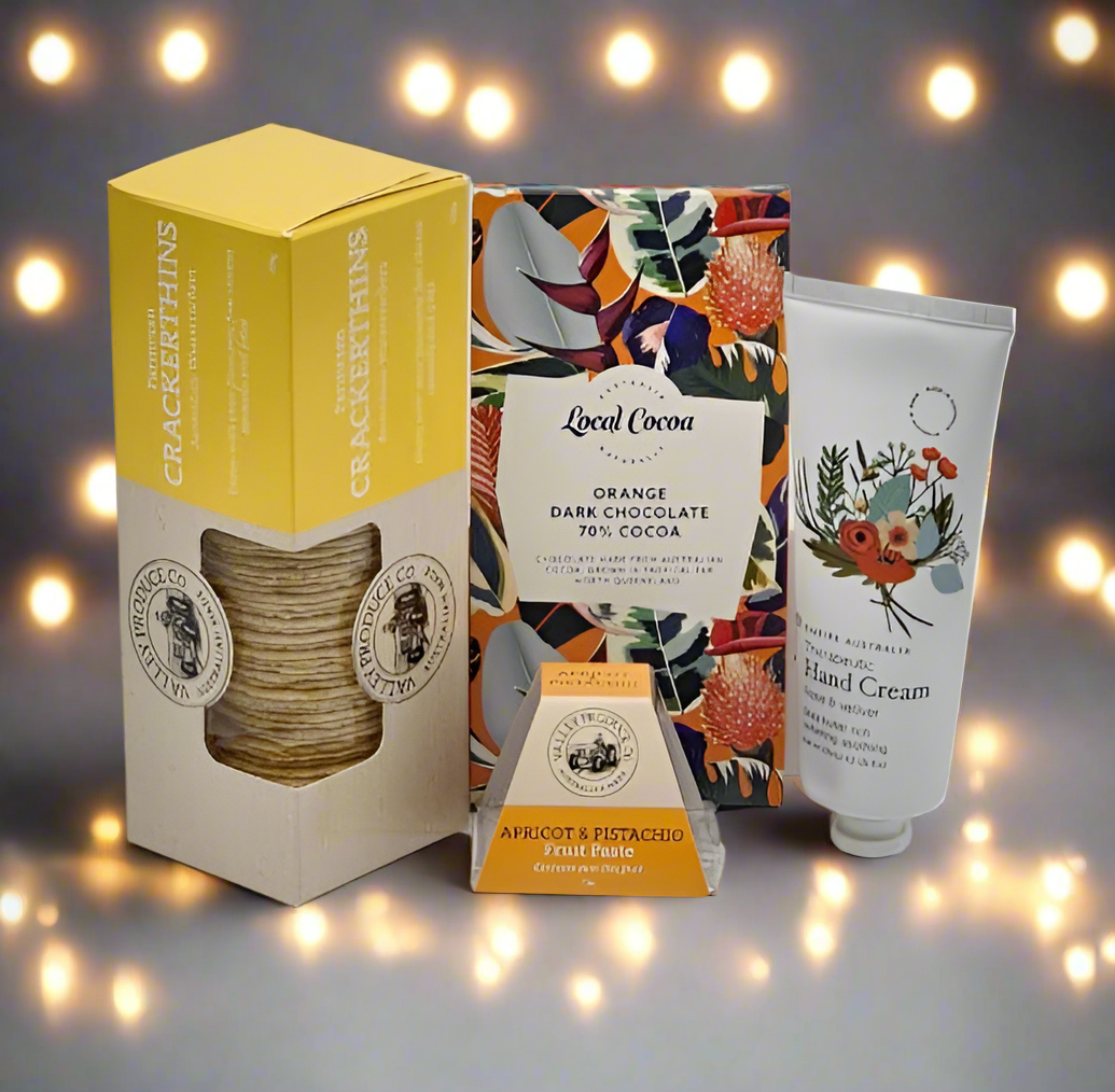 Collection of Crackerthins products including a box, chocolate bar, and hand cream against a softly blurred background with lights.