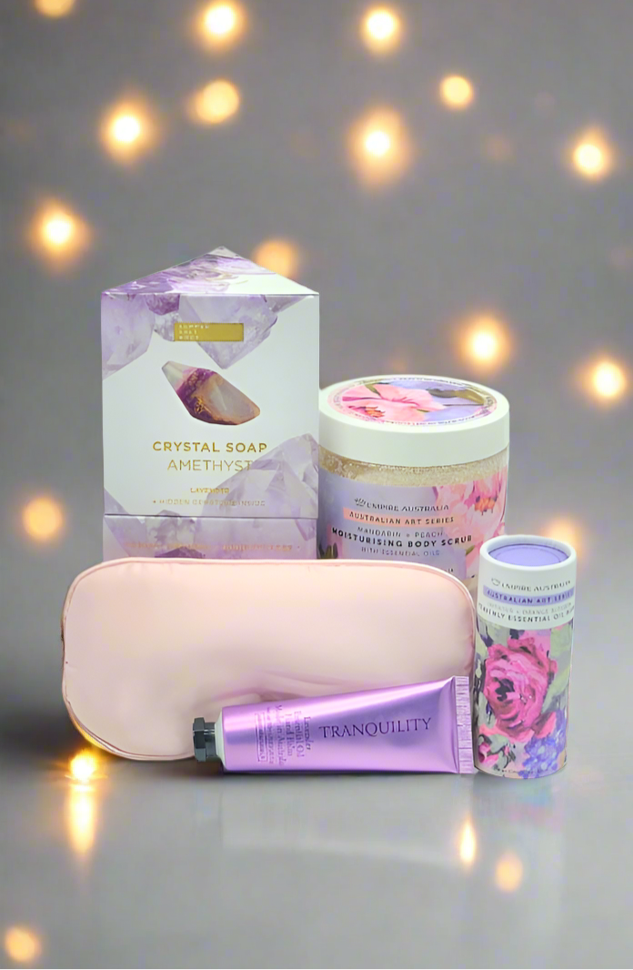 Collection of beauty products including a candle, soap, and lotion on a reflective surface with a softly blurred background.