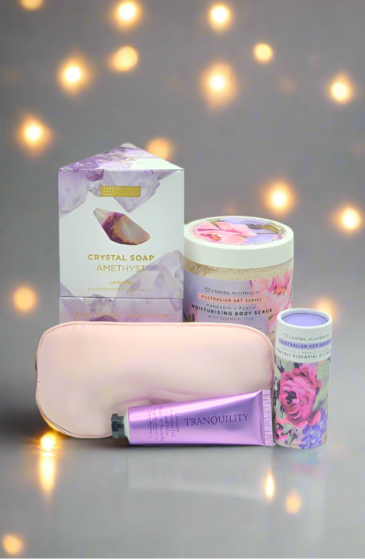 Collection of beauty products including a candle, soap, and lotion on a reflective surface with a softly blurred background.