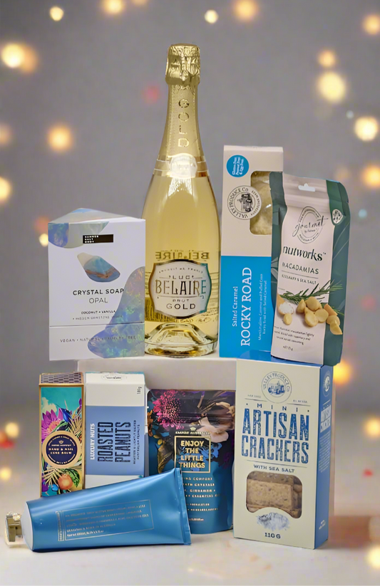 Assorted gourmet food and drink items including a bottle of champagne and packaged snacks on a blurred background.