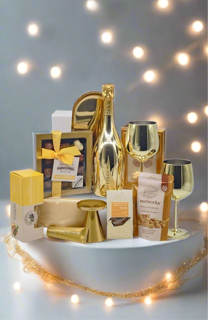 Gourmet gift basket with champagne, snacks, and glasses on a decorative stand with string lights.